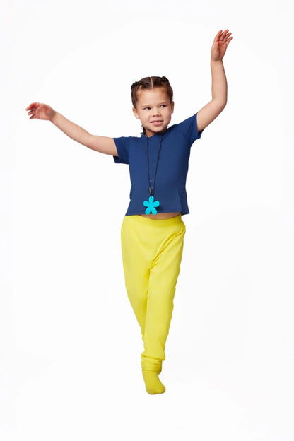 Child in sensory-friendly blue shirt, yellow pants, and teal chewelry necklace posing playfully