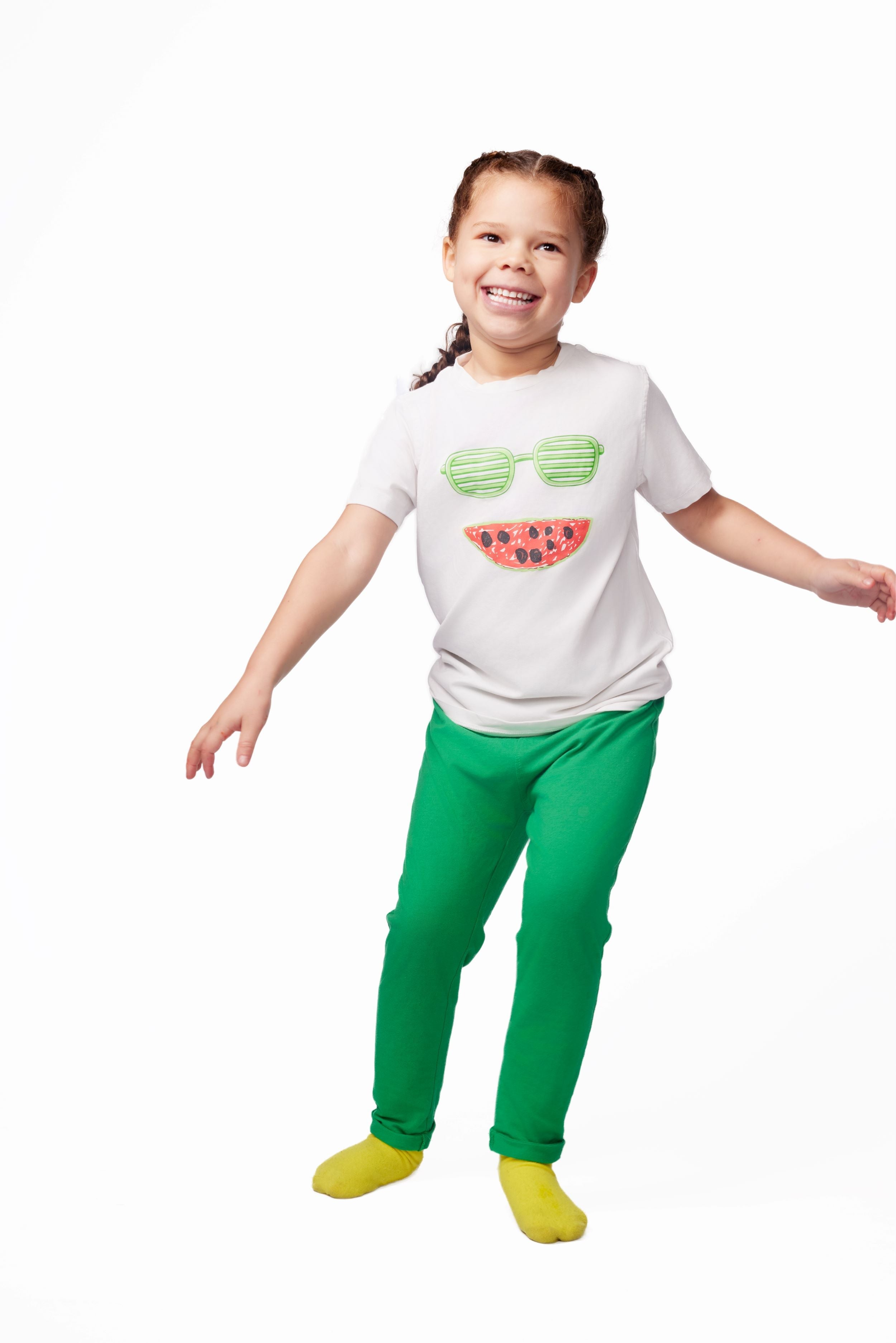 Child wearing a white t-shirt with sunglasses and watermelon design and green pants on a white background