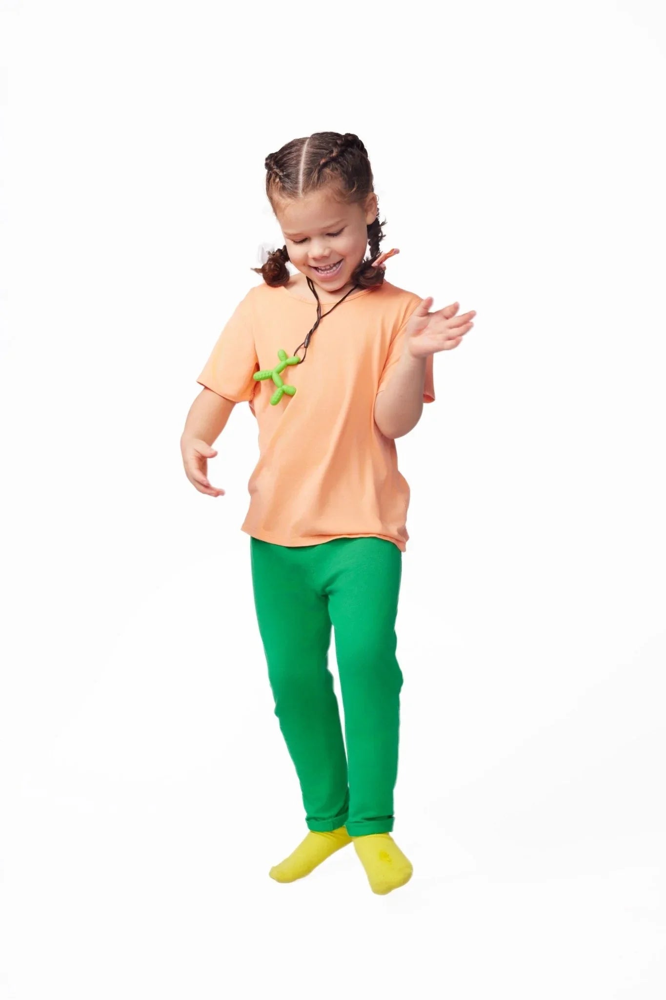 Smiling child in sensory-friendly orange shirt, green pants, and yellow socks with green fidget necklace