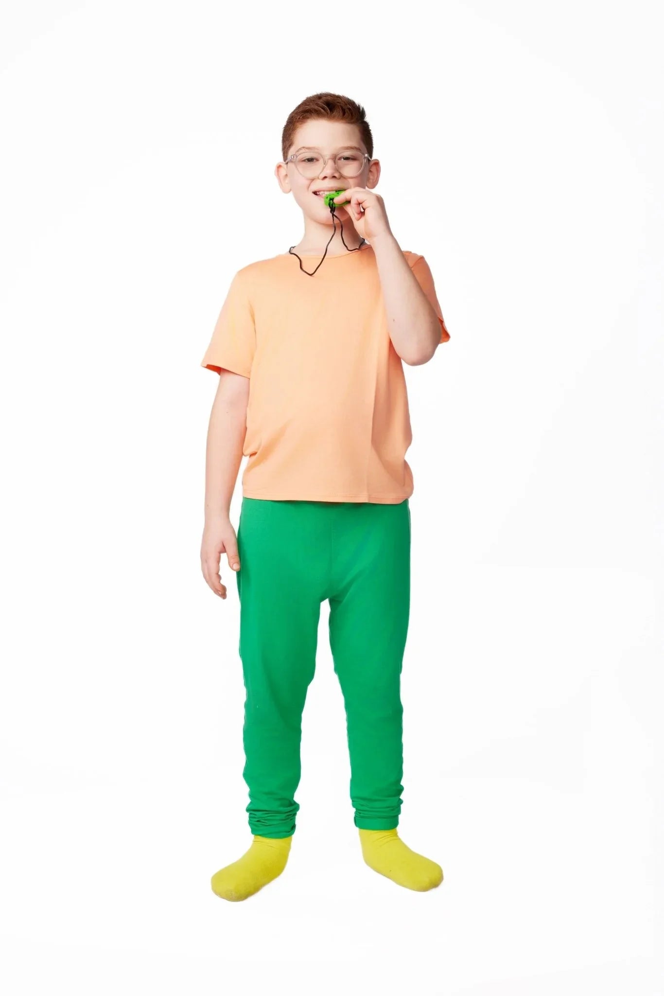 Child wearing sensory-friendly clothing, peach shirt and green pants, with a chewable necklace.