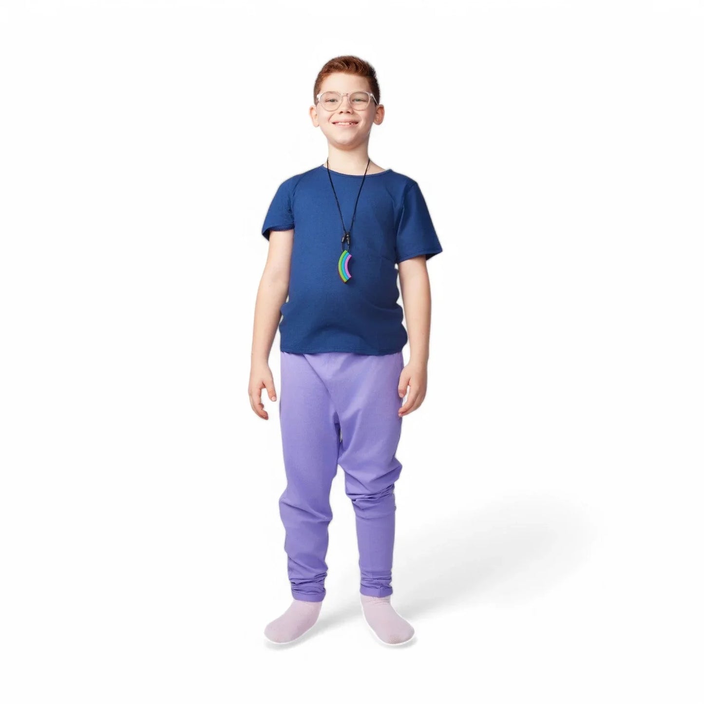 Smiling child wearing glasses, a blue shirt, purple sensory-friendly pants, and a rainbow chew necklace