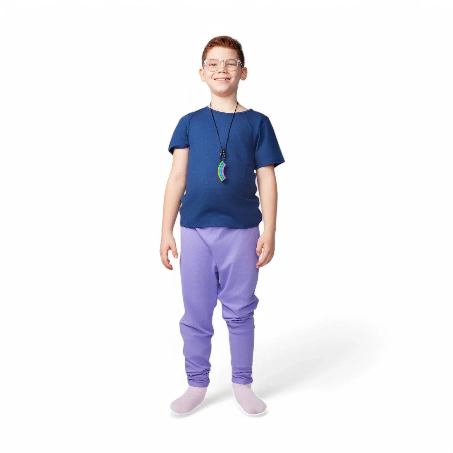 Smiling child wearing glasses, a blue shirt, purple sensory-friendly pants, and a rainbow chew necklace