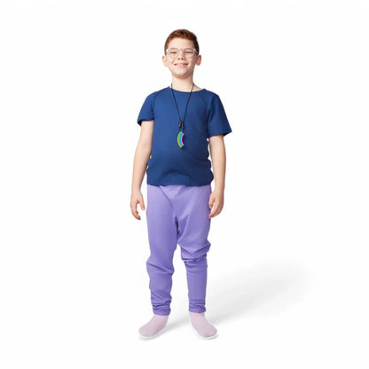 Smiling child wearing glasses, a blue shirt, purple sensory-friendly pants, and a rainbow chew necklace