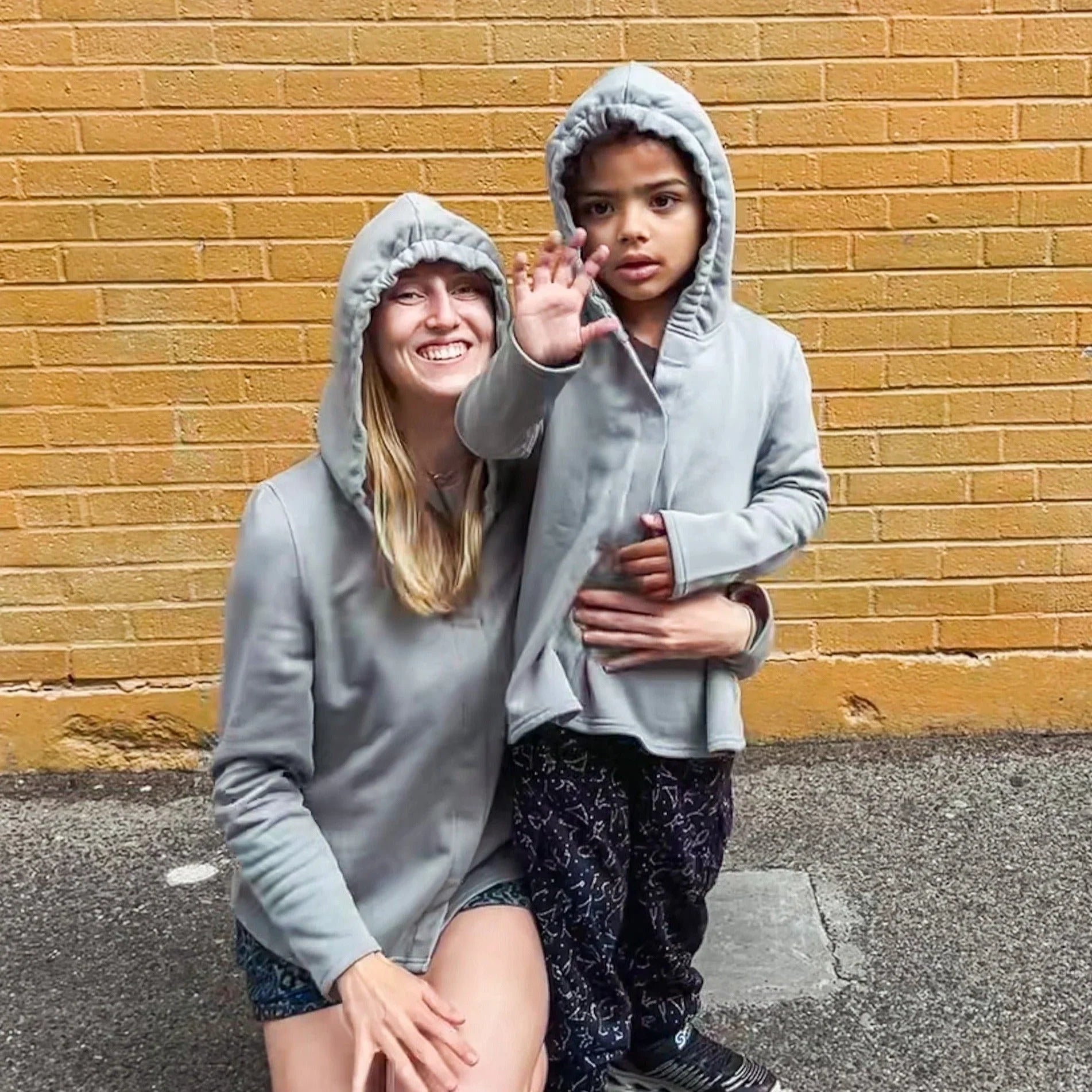 Adult and child wearing sensory-friendly gray hoodies in front of a yellow brick wall