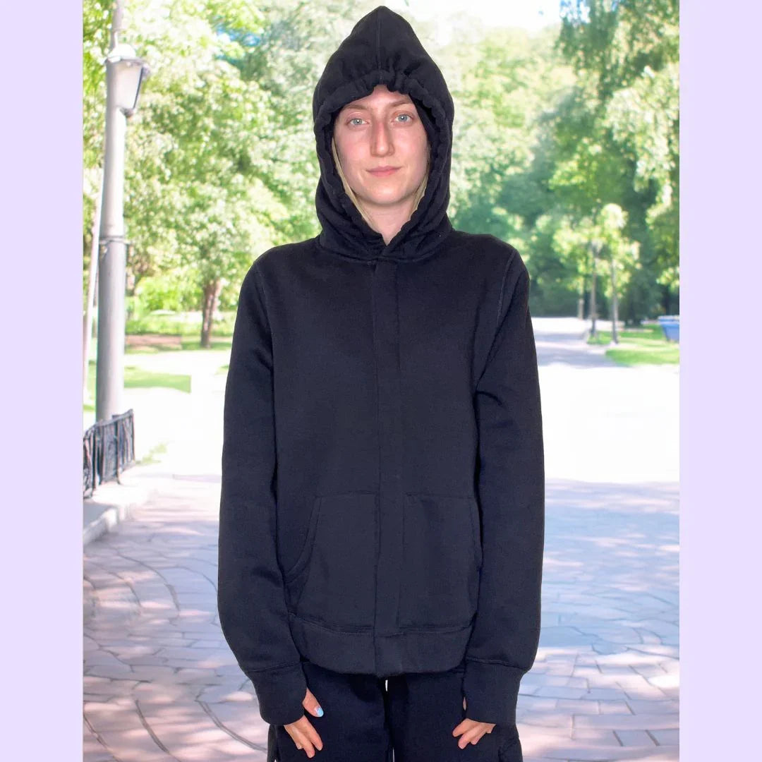 Person in sensory-friendly black hoodie with hood up, standing outdoors in a park