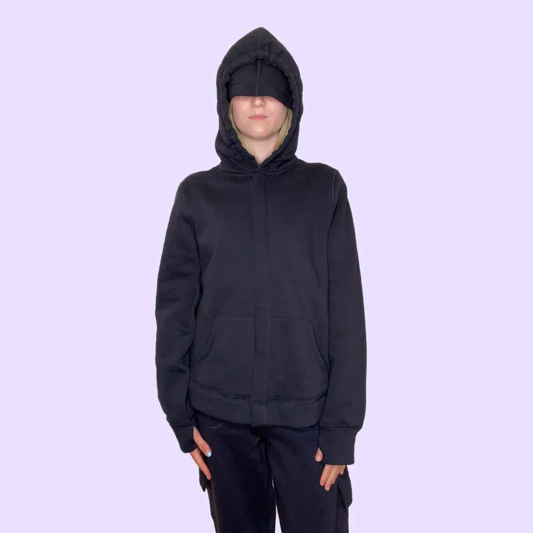 Person wearing sensory-friendly black hoodie with hood and eye mask on light purple background