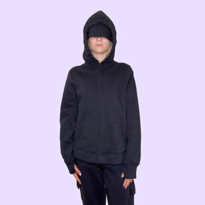 Person wearing sensory-friendly black hoodie with hood and eye mask on light purple background