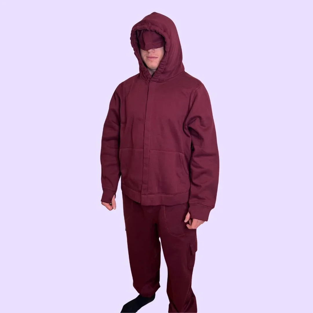 Person wearing sensory-friendly maroon hoodie and pants set with eye cover, lavender background