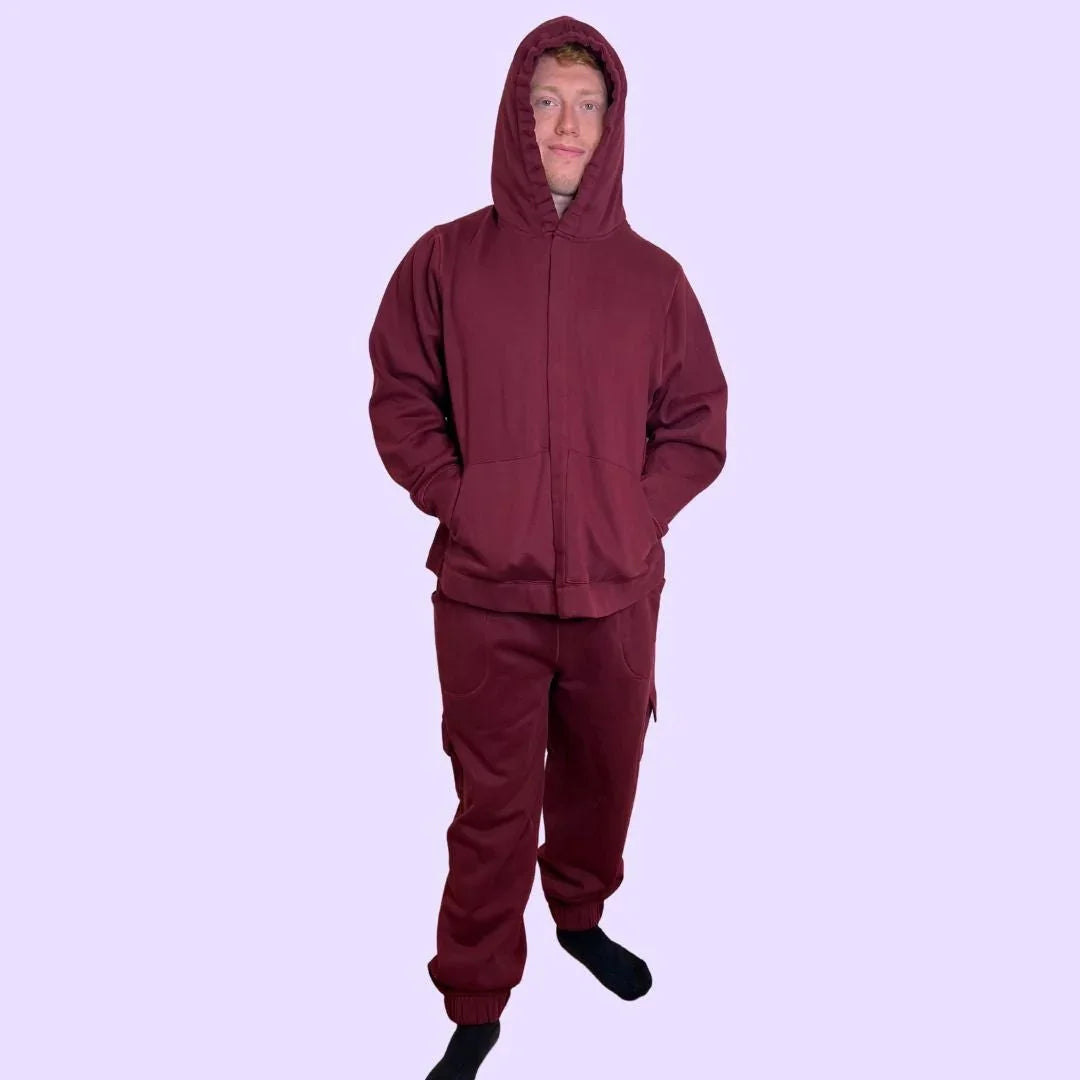 Adult wearing maroon sensory-friendly joggers and hoodie, standing on light purple background.