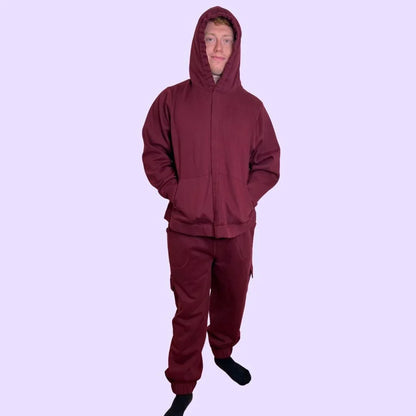 Adult wearing maroon sensory-friendly joggers and hoodie, standing on light purple background.