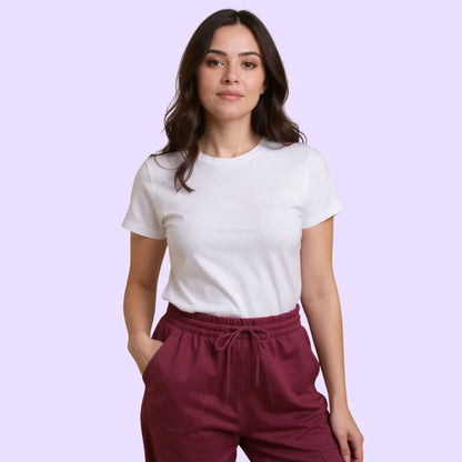 Woman wearing sensory-friendly white t-shirt and maroon pants, hands in pockets, on light purple background.