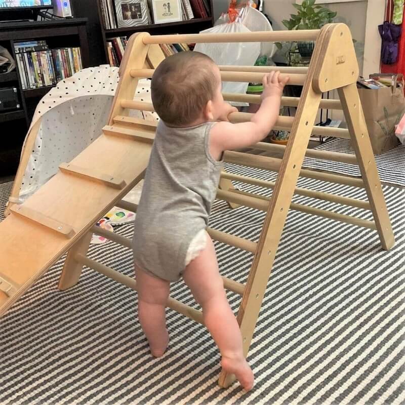 Baby climbing a wooden play structure on a striped rug