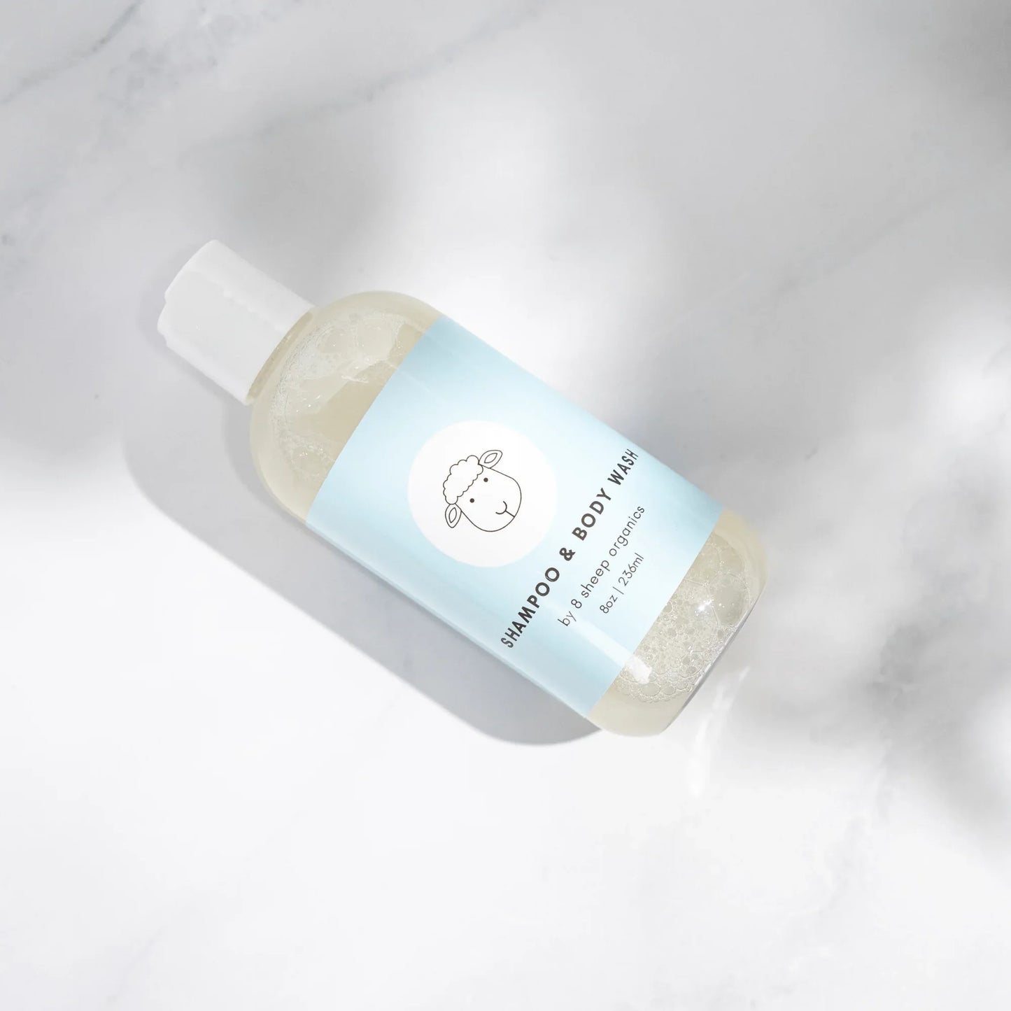 Gentle organic shampoo and body wash bottle with sheep logo on light blue label, marble background