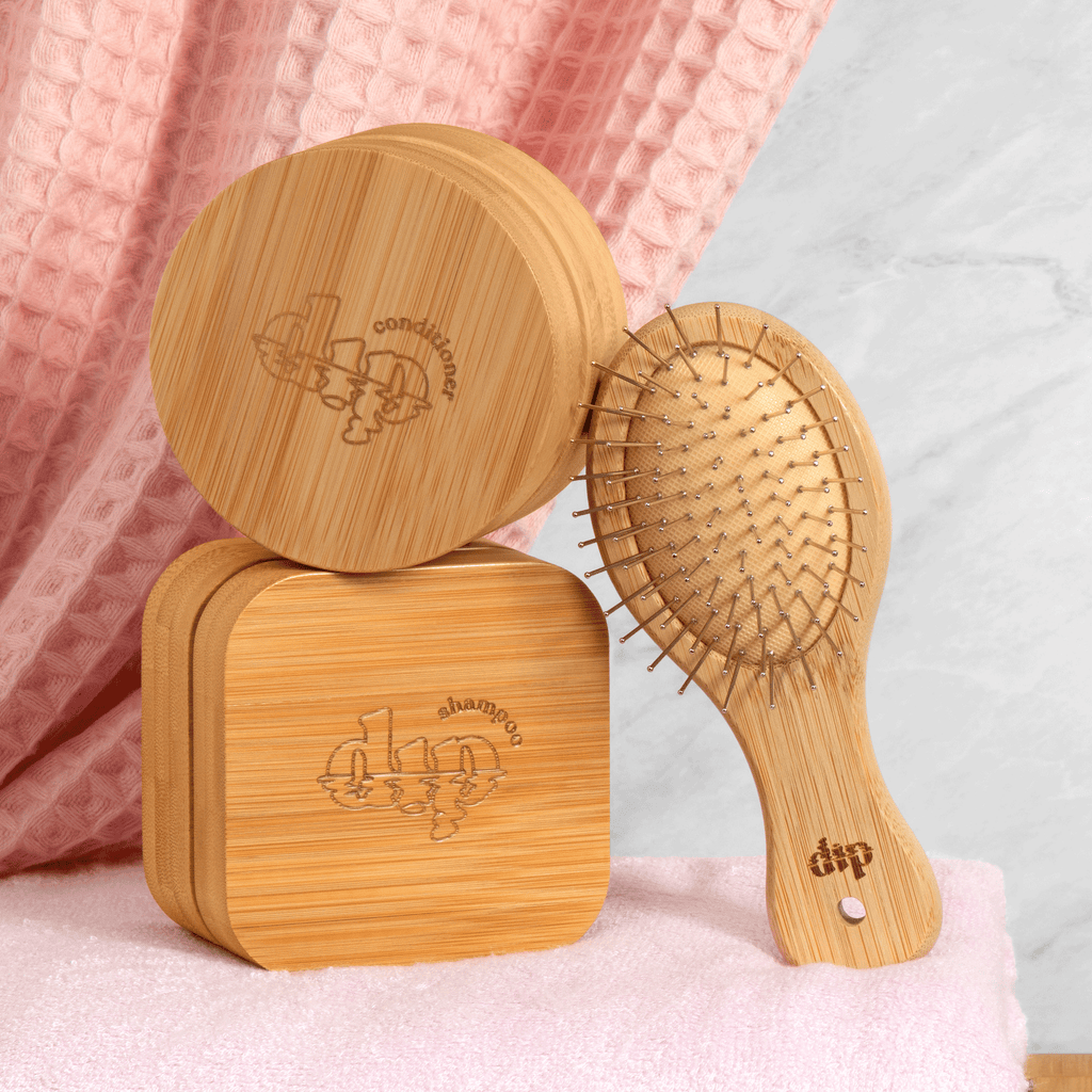Wooden hairbrush and its packaging on a pink surface with a light gray background