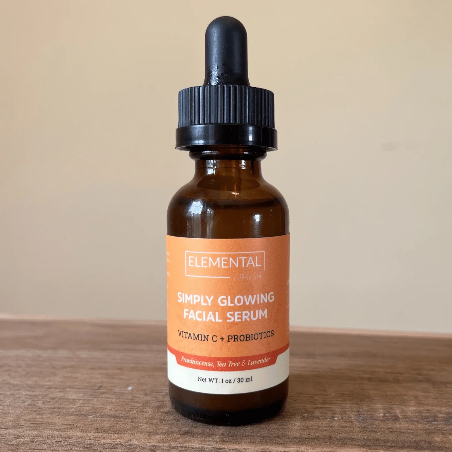 Amber dropper bottle of Simply Glowing Facial Serum with Vitamin C and probiotics on wood surface