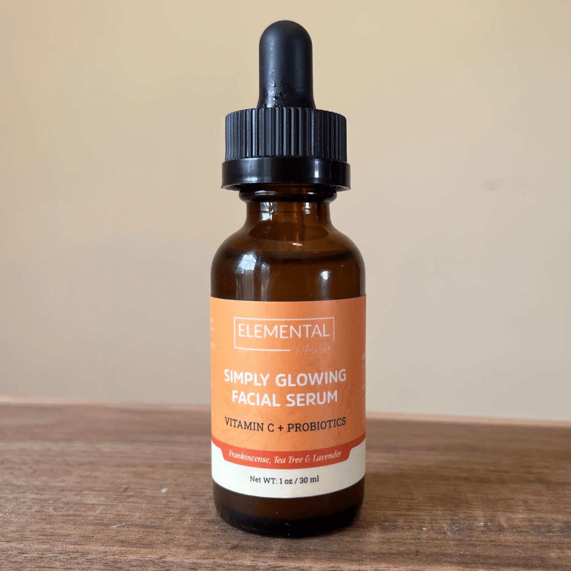 Amber dropper bottle of Simply Glowing Facial Serum with Vitamin C and probiotics on wood surface