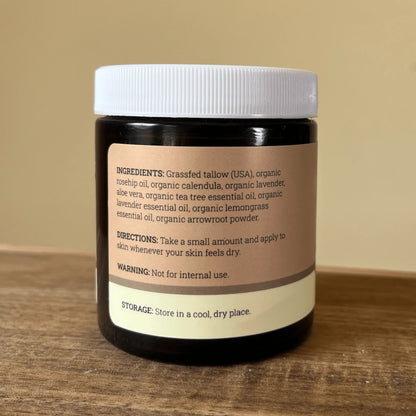 Jar of whipped tallow balm with natural, organic ingredients label on wooden surface