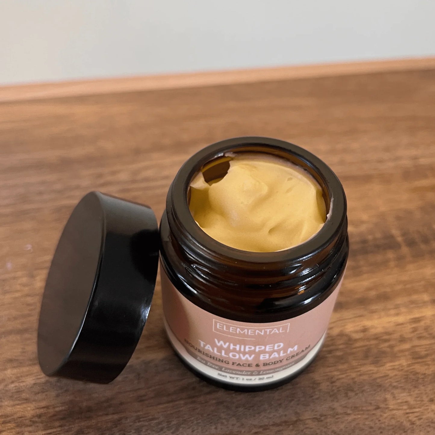 Open jar of whipped tallow balm with creamy yellow texture on a wooden surface