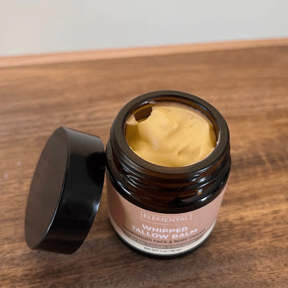 Open jar of whipped tallow balm with creamy yellow texture on a wooden surface