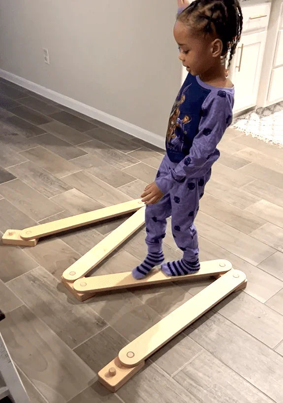 Child balancing on wooden W-shaped sensory balance beam in indoor play area