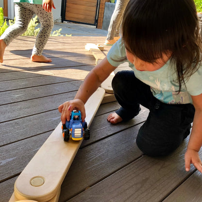 Child playing with toy car on wooden sensory balance board outdoors