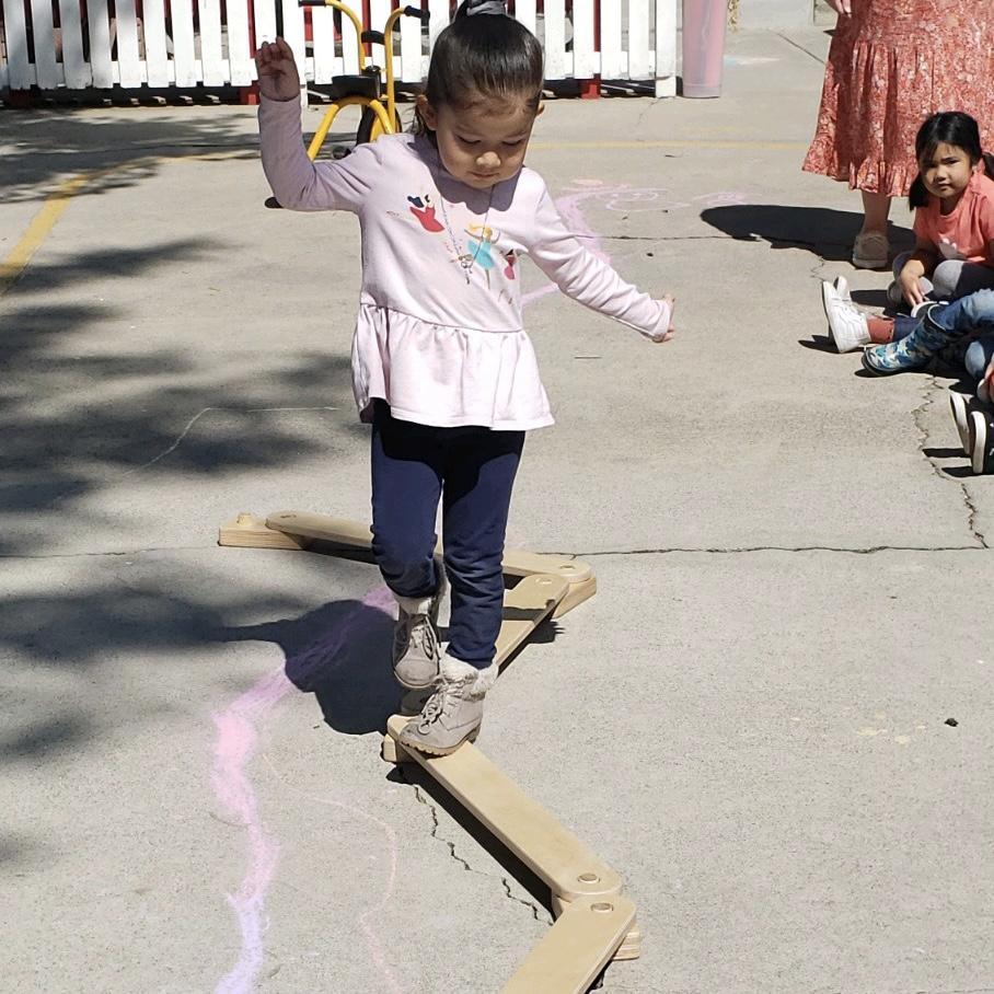 Young girl balancing on a sensory motor pathway outdoors, surrounded by children.