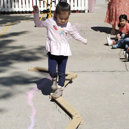 Young girl balancing on a sensory motor pathway outdoors, surrounded by children.