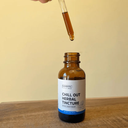 Amber glass bottle labeled Chill Out Herbal Tincture with dropper above on wooden surface