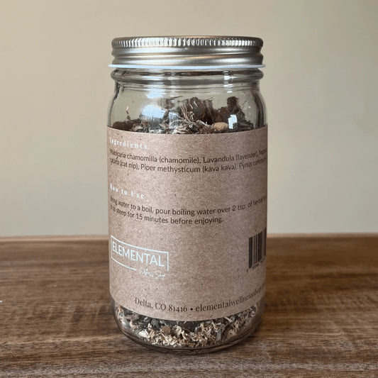 Glass jar of loose leaf herbal tea blend for relaxation on wooden table with ingredient label.