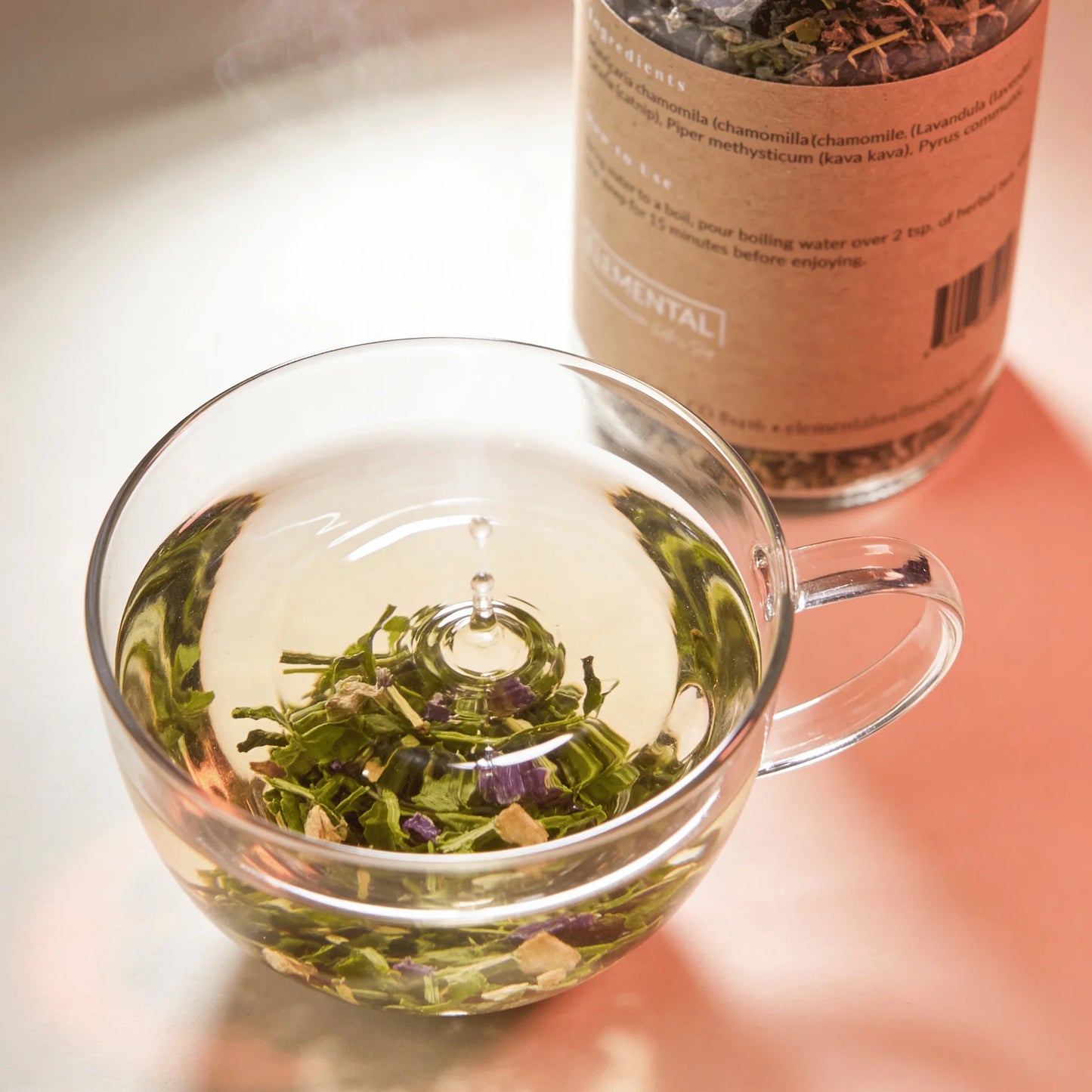 Glass cup of herbal tea with loose leaf blend, jar of loose leaf herbs in background