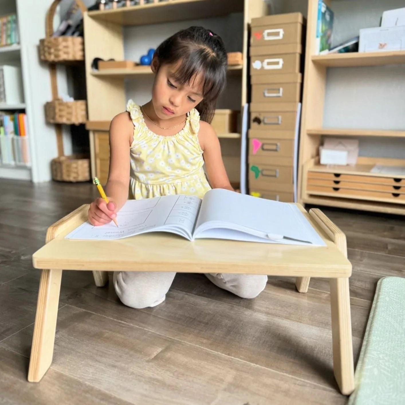 Young child using a wooden lap desk to write in a workbook, in a sensory-friendly home learning space.