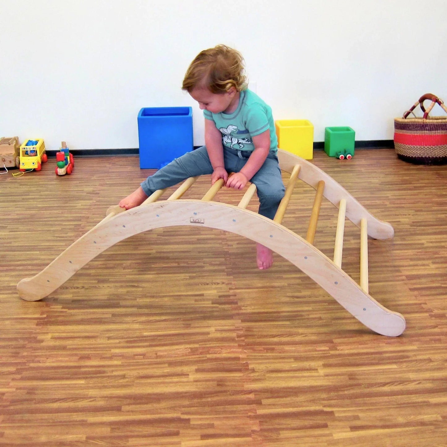 Child climbing on wooden Pikler arch in playroom with sensory-friendly toys