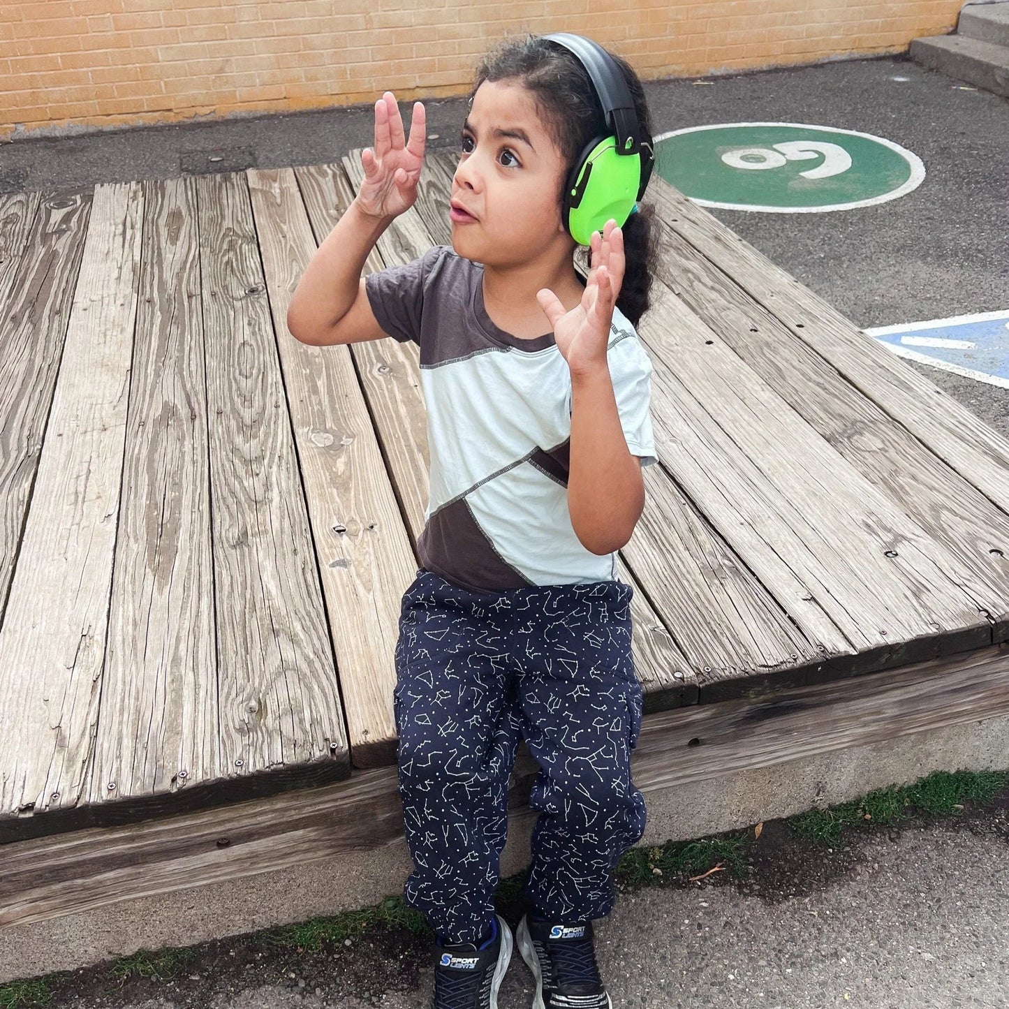 Child wearing noise-reduction headphones sitting outdoors on wooden platform
