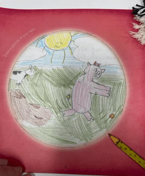 Children's drawing in a blank book featuring a pig and cow in a grassy field under a sunny sky.