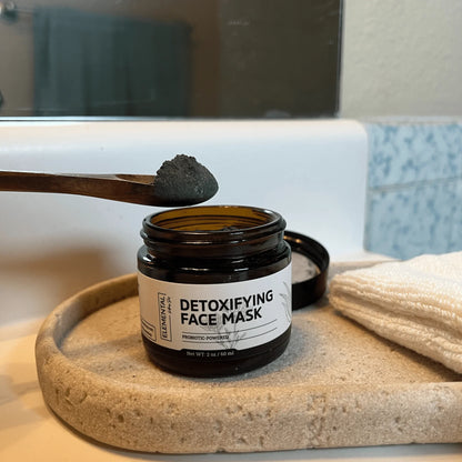 Detoxifying face mask powder in open jar with wooden spoon on bathroom tray