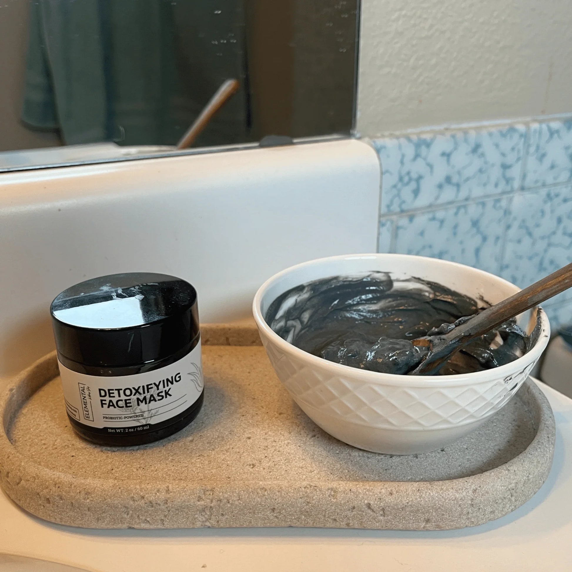 Detoxifying face mask jar and mixed clay mask in a bowl on bathroom counter