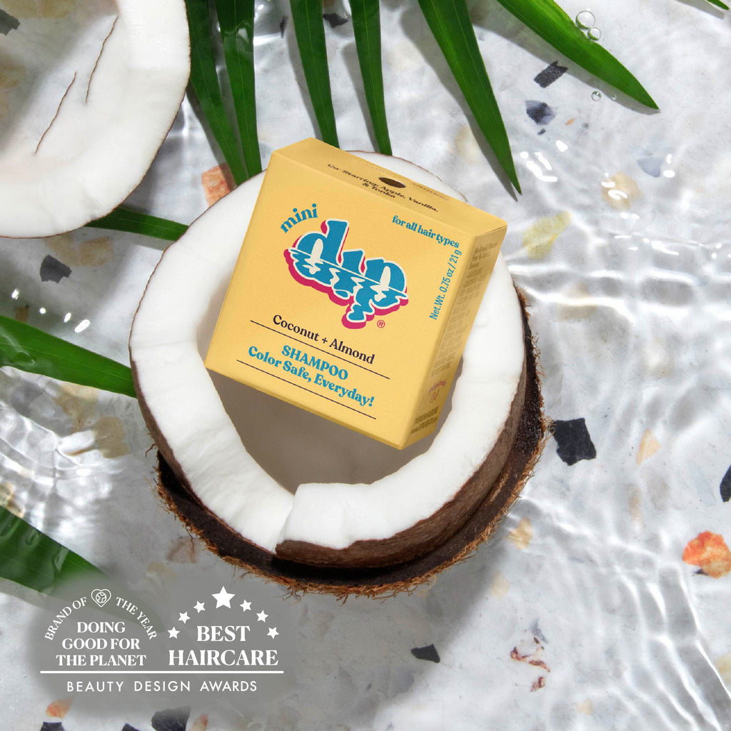 Box of shampoo inside a coconut with green leaves on a textured surface