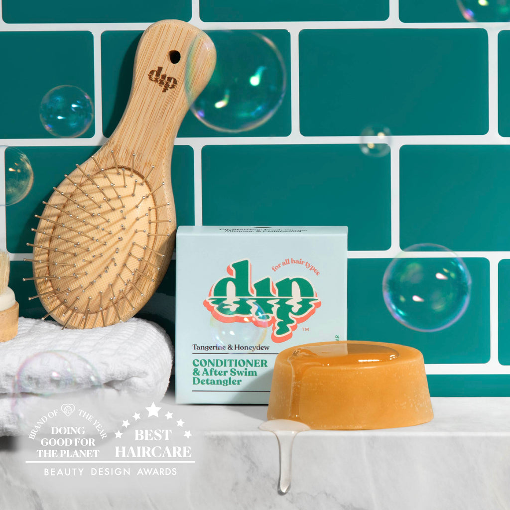 Bamboo hairbrush, soap, and box with 'dip' branding against a teal tiled wall.
