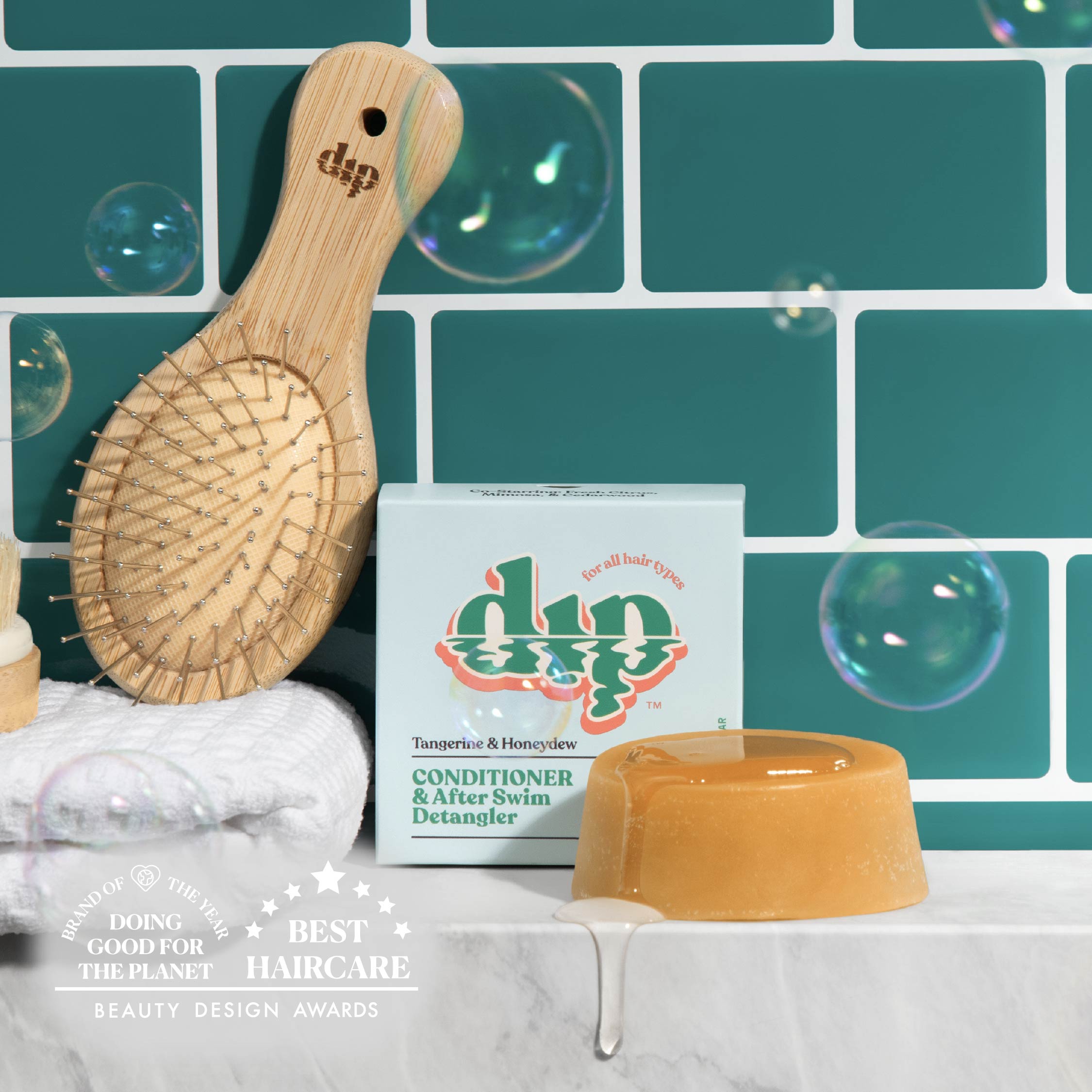 Bamboo hairbrush, soap, and box with 'dip' branding against a teal tiled wall.