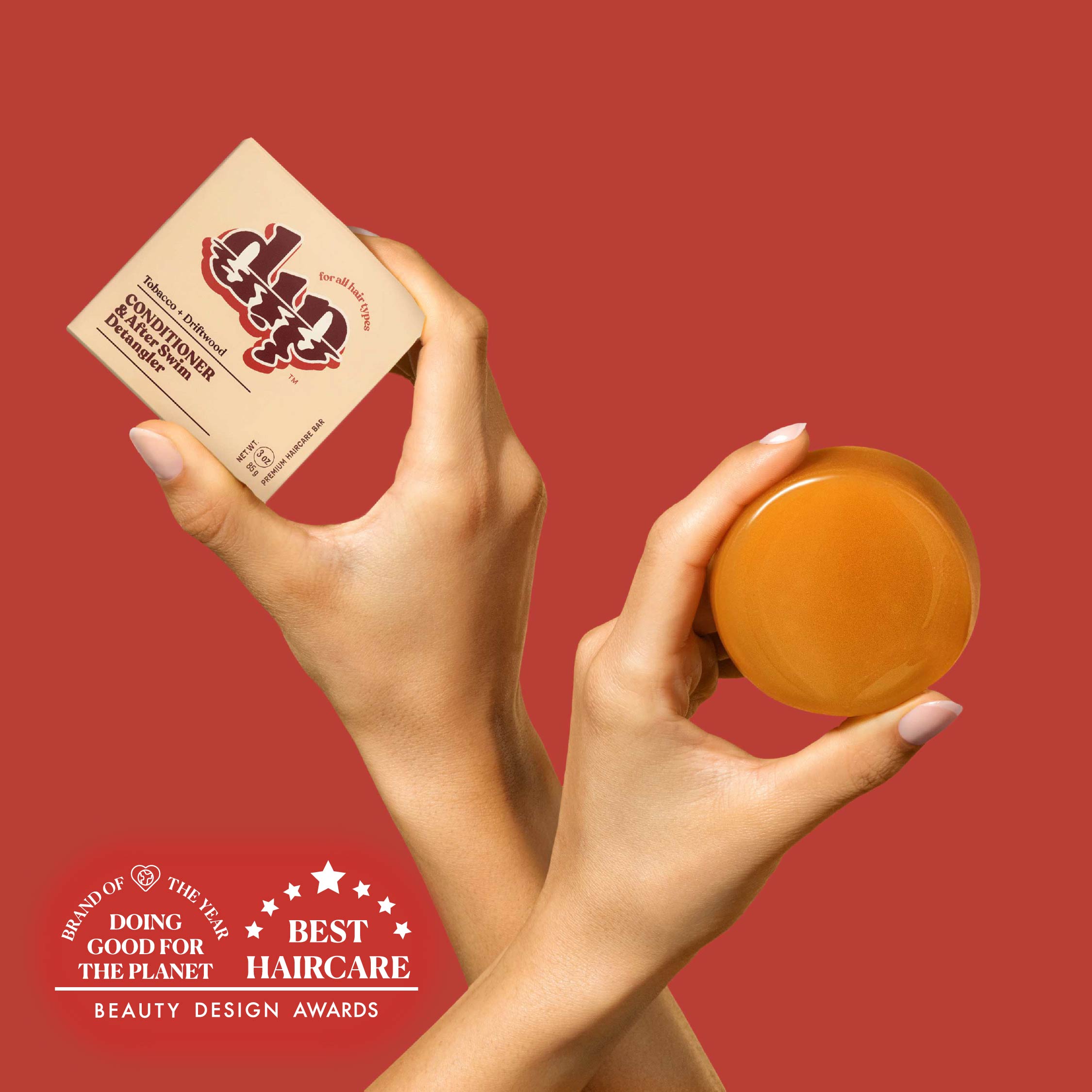 Hands holding a jar of hair product and a box against a red background with awards text.
