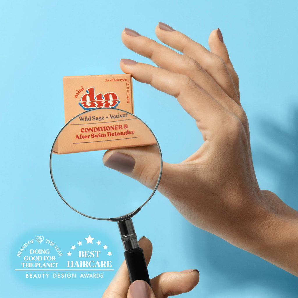 Hand holding a box of 'minidip' conditioner with a magnifying glass against a blue background