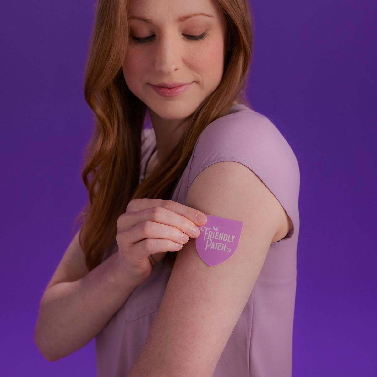 Woman applying a purple patch with text on her arm against a purple background