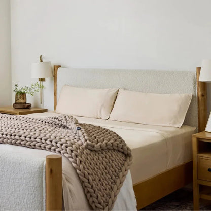 Beige chunky knit cooling weighted blanket on a neatly made bed in a cozy bedroom.