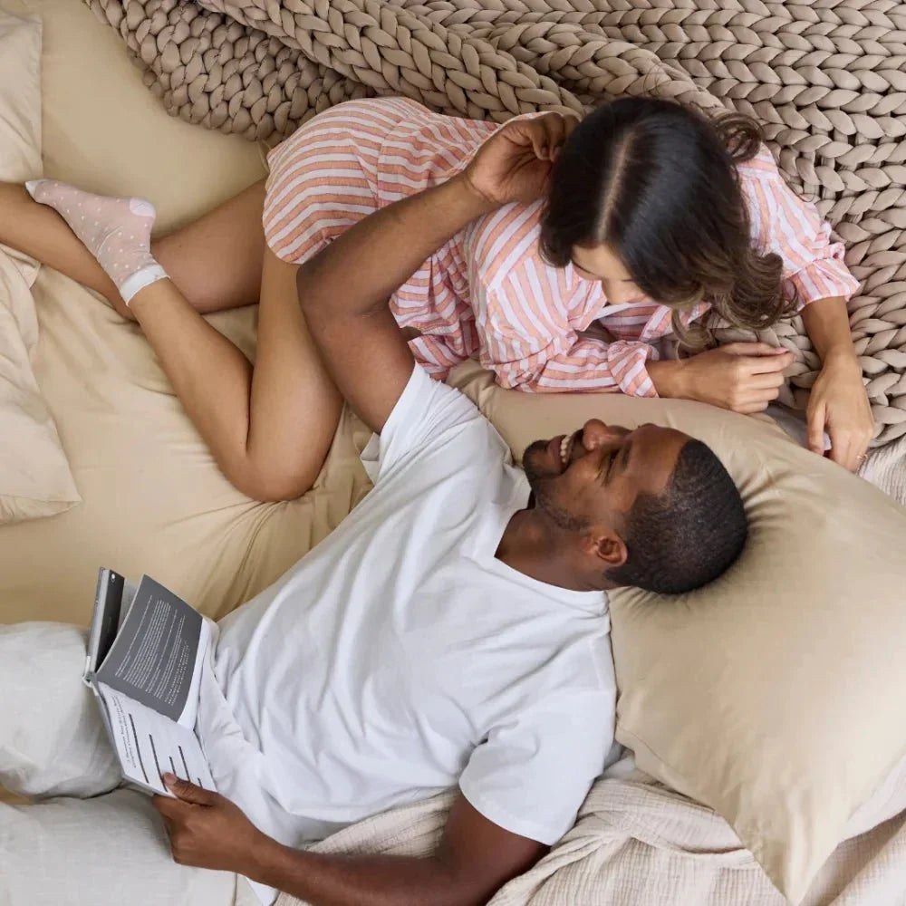 Couple relaxing on bed with chunky knit cooling weighted blanket in beige