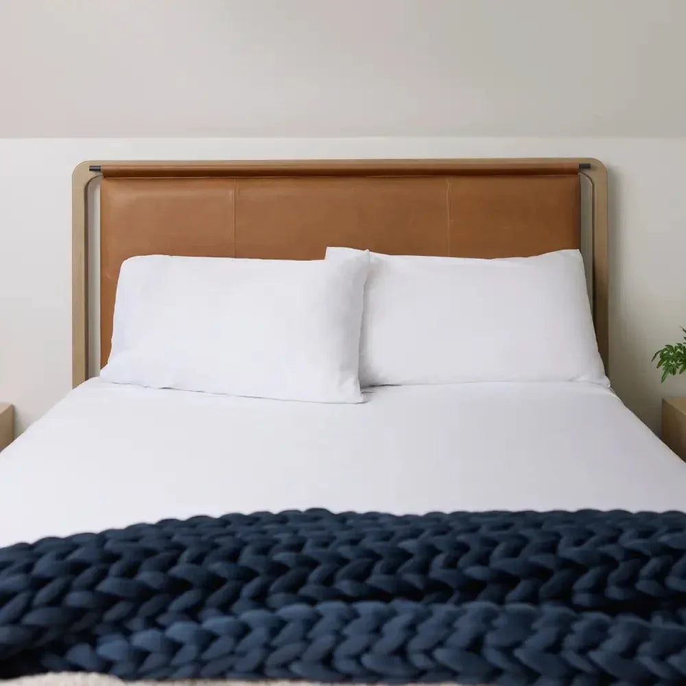 Cozy bed with white bedding and a chunky navy knit weighted blanket at the foot