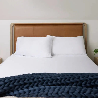 Cozy bed with white bedding and a chunky navy knit weighted blanket at the foot