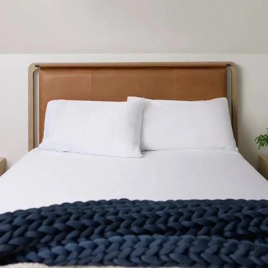 Cozy bed with white bedding and a chunky navy knit weighted blanket at the foot