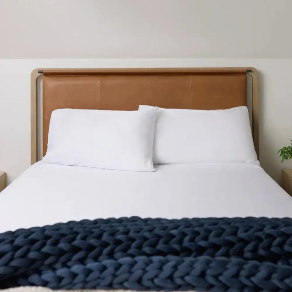 Cozy bed with white bedding and a chunky navy knit weighted blanket at the foot