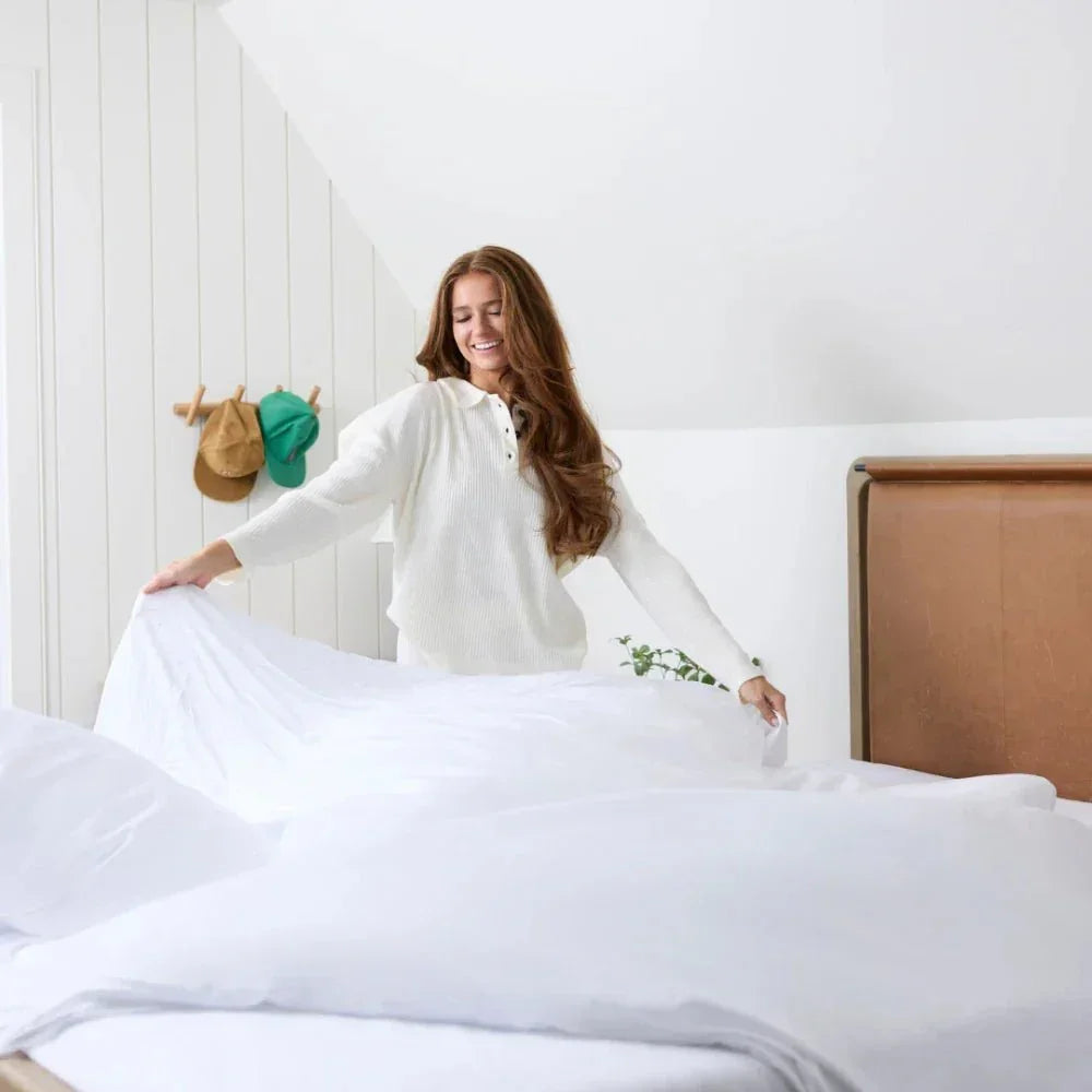 Woman making bed with white cooling weighted blanket in bright bedroom