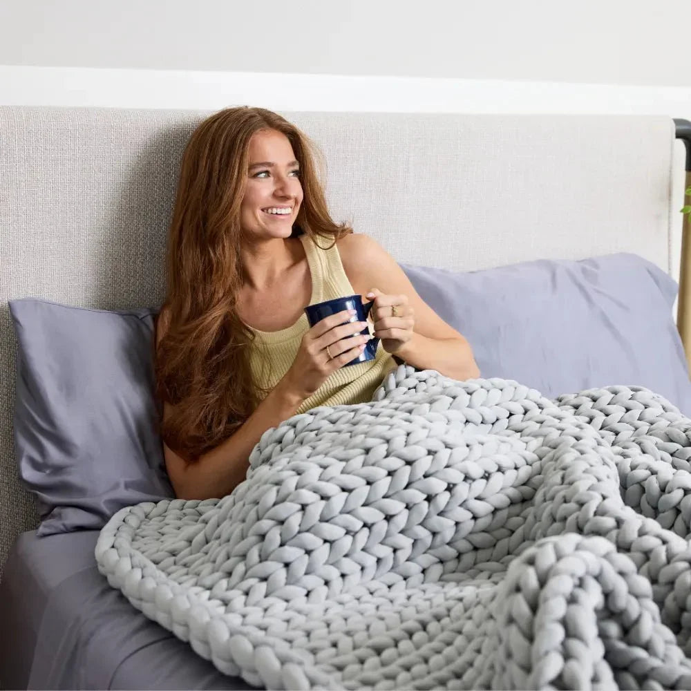 Woman relaxing in bed with chunky knit cooling weighted blanket in arctic grey